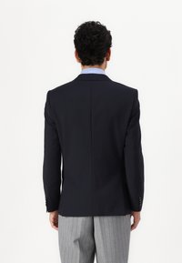 Σακάκι ναυτικού τύπου με εφαρμογή, μονό άνοιγμα και παντελόνια με λοξές καμπύλες σε ανοιχτό γκρι με ρίγες. Λείο υλικό.