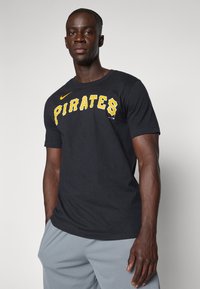 Camiseta de algodón negra con la palabra "PIRATES" en letras amarillas en negrita, logo de Nike en amarillo y un escote redondo estándar.
