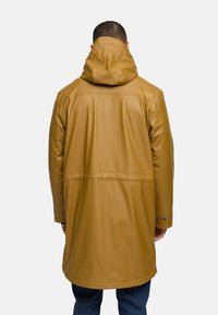 Impermeabile giubbotto giallo senape con cappuccio, materiale resistente, taglio lungo e cuciture a contrasto lungo la schiena e le maniche.