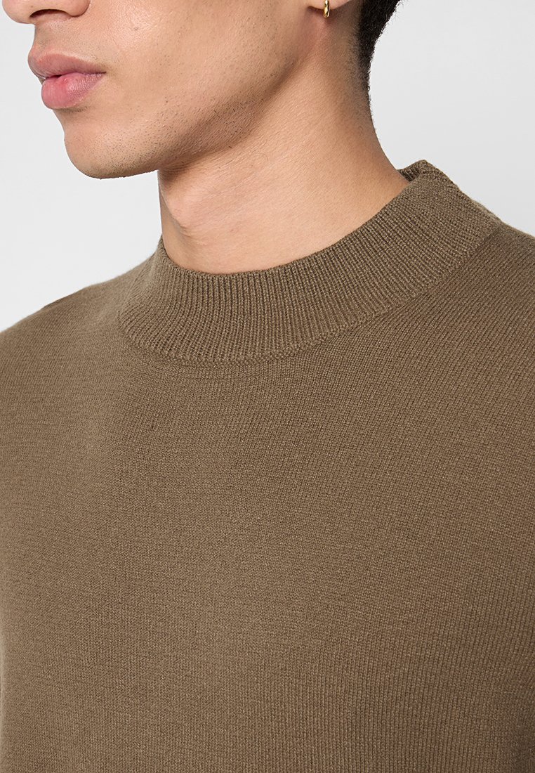 Brauner, gestrickter Pullover mit hohem, geripptem Kragen und glatter Textur, entworfen für eine taillierte Passform ohne sichtbare Muster oder Hardware.