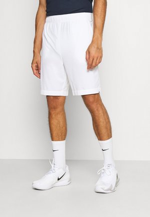 Shorts blancs avec une taille élastique, ourlet plat, poches latérales, portés avec des chaussettes et des chaussures Nike blanches ornées d'un logo swoosh noir.