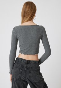 Crop top grigio a maniche lunghe con un orlo ondulato, abbinato a jeans scuri a vita alta grigio. Presenta un design aderente e un tessuto testurizzato.