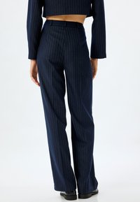 Marineblauwe pinstripe broeken met een rechte snit, voorzien van een tailleband en een gladde textuur, gecombineerd met een cropped top.