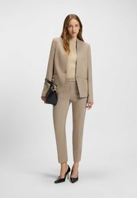Beige op maat gemaakt pak met een gestructureerde blazer en slanke broek. Gecombineerd met een geribbelde lichtbruine top en zwarte puntige hakken.