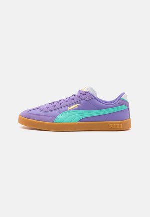 Baskets Puma violettes avec une bande bleu sarcelle, une semelle gomme et des logos Puma jaunes, vues de côté sur un fond blanc uni.