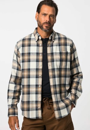Flannelskjorte i creme, marineblå og tan rute mønster. Har knaplukning foran, krave og lange ærmer, båret over en sort skjorte.