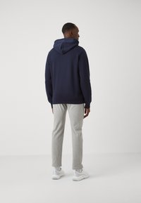 Jūras spēku hoodie ar aukliņu kapuci, apvienots ar gaiši pelēkiem sporta biksēm un baltām kedām. Mīksts audums ar brīvu piegriezumu.