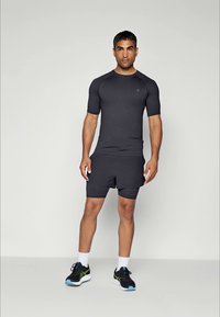 T-shirt de sport à manches courtes gris foncé assorti avec un short, présentant une coupe slim et une texture lisse. Des baskets noires et vertes complètent le look.