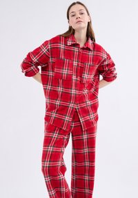 Czerwona koszula flanelowa w kratę z dwoma kieszeniami na piersi, zapięcie na guziki i podwiniętymi rękawami, w połączeniu z dopasowanymi spodniami w kratę. Miękka tekstura.