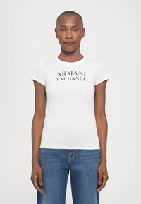 Hvit tettsittende t-skjorte med korte ermer, med "ARMANI EXCHANGE" logo i svart skrift over brystet. Bært sammen med blå jeans.