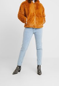 Falešná kožešinová bunda v spáleně oranžové, na zip, se dvěma kapsami. Světle modré skinny džíny. Ankle boots s hadím potiskem v černé a šedé barvě.