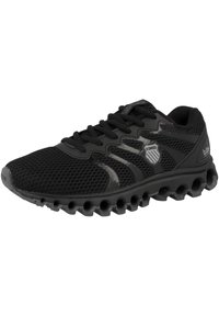Scarpa da ginnastica nera con tomaia in rete, dettagli sintetici e suola testurizzata con fori circolari per flessibilità e aderenza.