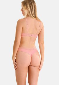 Ensemble de lingerie rose poussiéreux comprenant un bralette avec des bretelles ajustables et des ornements décoratifs, accompagné d'un string taille basse assorti. Texture lisse.