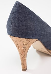 Chaussure à talon haut en tissu bleu marine avec talon en liège texturé et détail arrière pointu sur fond blanc.
