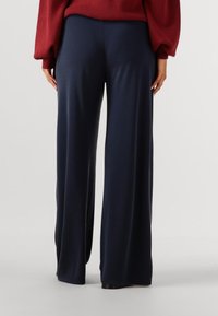 Pantaloni a gamba larga in tessuto blu navy scuro, con una texture liscia e una vestibilità comoda, dotati di una vita pulita e senza dettagli hardware visibili.