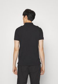 Camiseta polo negra de manga corta, con cuello y dobladillo recto. Textura suave y diseño minimalista.