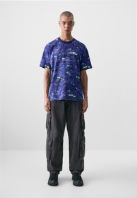 Purple short-sleeve shirt with a blue and green abstract design, paired with dark cargo pants and black sneakers.