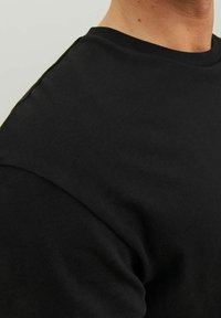 Svart t-shirt med kort ärm, tillverkad av slätt tyg, med rund halsringning och sydda axelsömmar som framhäver dess enkla design.