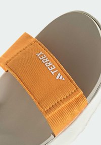 Σανδάλι Terrex slide με φαρδιά πορτοκαλί υφασμάτινη λωρίδα, επενδεδυμένη μπεζ σόλα και λευκή σόλα, με λεπτομέρεια λογότυπου στη λωρίδα.