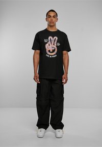 Sort bomulds T-shirt med farverig fredssymbol grafik og teksten "LEV I FRED." Sættes sammen med løse sorte cargo bukser og hvide sneakers.