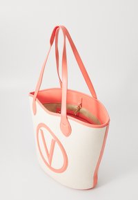 Tote bag gemaakt van crèmekleurig textuurmateriaal met koraal nepleeraccenten en een groot rond logo. Heeft twee lange handvatten en een binnenzak met rits.