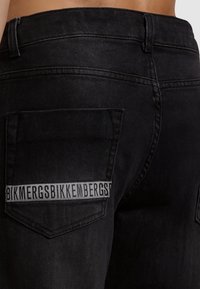 Jeans in denim nero con una tasca posteriore dotata di un'etichetta in tessuto che riporta la scritta "BIKKEMBERGS". Il design presenta una vestibilità classica e una texture sottile.