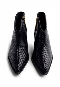 Pair of black woven leather pointed-toe ankle boots with gold side zippers, viewed from the front on a white background.