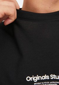 Schwarzes Baumwoll-T-Shirt mit rundem Halsausschnitt und kurzen Ärmeln. Auf der Vorderseite sind weiße Drucktexte zu sehen. Glatte Textur.