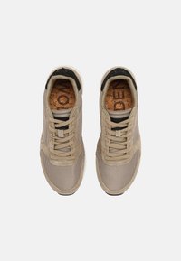 Beige nät- och mockaskor med rundad tå, platta snören och en texturerad korkinlägg. Vit gummisula med svarta accenter.