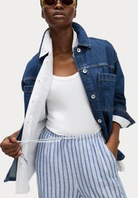 Denimjakke med knaplukninger over en hvid tanktop, parret med blå og hvide stribede bukser med elastisk talje og snor.