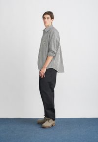 Camisa de botones a rayas en blanco y negro, de corte relajado, combinada con pantalones negros y botas de ante grises, con suelas de goma.