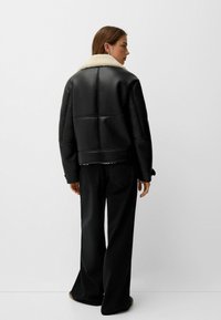 Jachetă din piele neagră cu guler din blană albă, având un design scurt și textură matlasată, asortată cu pantaloni largi negri.