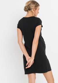 Abito nero a maniche corte realizzato in tessuto morbido. Presenta un semplice scollo rotondo e un dettaglio arricciato sul lato. Lunghezza sopra il ginocchio.