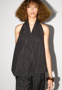 Zwarte haltertop met een wikkeldesign, met verticale strepenstructuur en gedrapeerde stof. Geaccentueerd door een gelaagde snit.