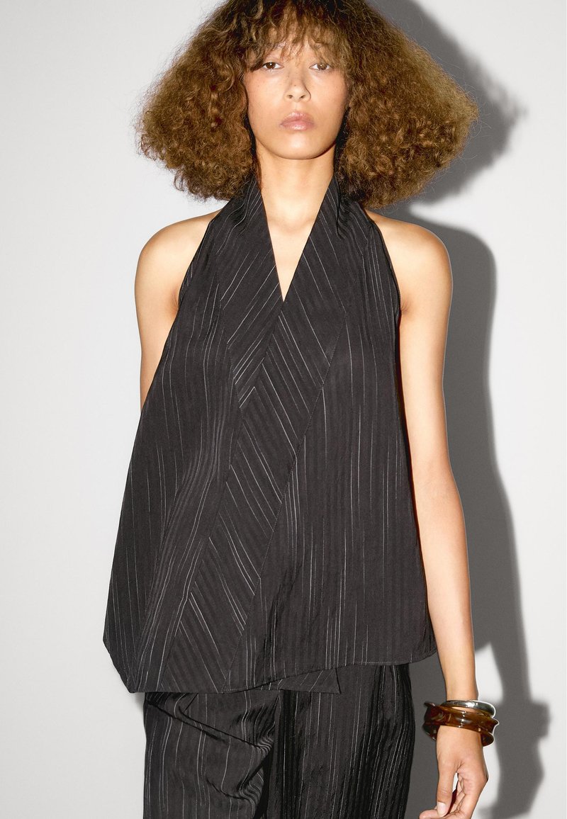 Zwarte haltertop met een wikkeldesign, met verticale strepenstructuur en gedrapeerde stof. Geaccentueerd door een gelaagde snit.