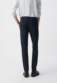 Marine casual broek met een tapered fit en een elastische tailleband, met twee achterzakken en gedragen met zwarte gestructureerde schoenen.