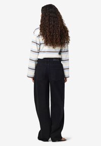 Ριγέ μακρυμάνικο πουκάμισο σε λευκό, μπλε και γκρι, συνδυασμένο με μαύρα φαρδιά τζιν. Το πουκάμισο έχει στρογγυλή λαιμόκοψη; τα τζιν διαθέτουν πίσω τσέπες.