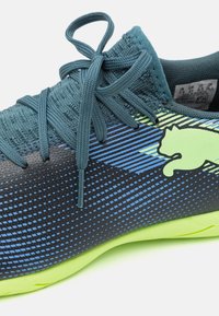 Zapatillas deportivas con una parte superior de malla con rayas en degradé de teal y azul, una entresuela negra texturizada y una suela exterior de goma verde brillante.