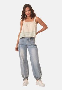 Top sin mangas de color crema con tela texturizada y bordado en verde menta; combinado con pantalones vaqueros holgados de color azul claro con puños recogidos.
