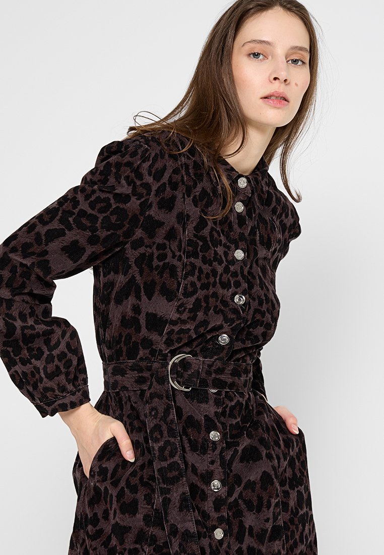 Abito in corduroy con stampa leopardata, vita con cintura, maniche lunghe e bottoni argentati lungo la parte anteriore. Schema di colori in viola scuro e nero.