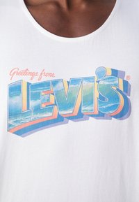 Gros plan sur une chemise blanche avec le texte coloré "Greetings from Levi's" comportant des graphismes de vagues océaniques à l'intérieur des lettres.