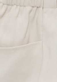 Gros plan sur un pantalon en tissu beige avec une taille élastique et une poche avant avec des détails de couture visibles.