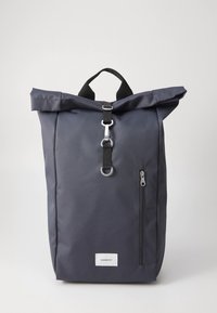 Mochila com fecho enrolado em tecido azul escuro com acabamento texturizado, bolso frontal com fecho de correr e um destacado fecho prateado.
