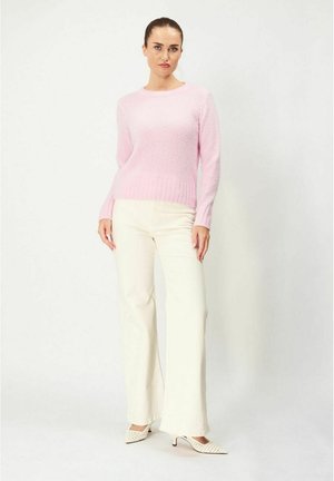 Vaaleanpunainen neulepaita, jossa on pyöreä kaula-aukko ja ribbireunus, yhdistetty valkoisiin leveälahkeisiin housuihin ja teräväkärkisiin valkoisiin korkokenkiin, joissa on reikärovotuksia.