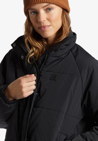 Sort pufferjakke med lynlås foran og tryklås. Med quilted design, stående krave og logo-lap på brystet.