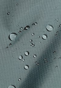 Vattenavvisande tyg i dämpad teal, med en texturerad yta där olika storlekar av droppar vilar.