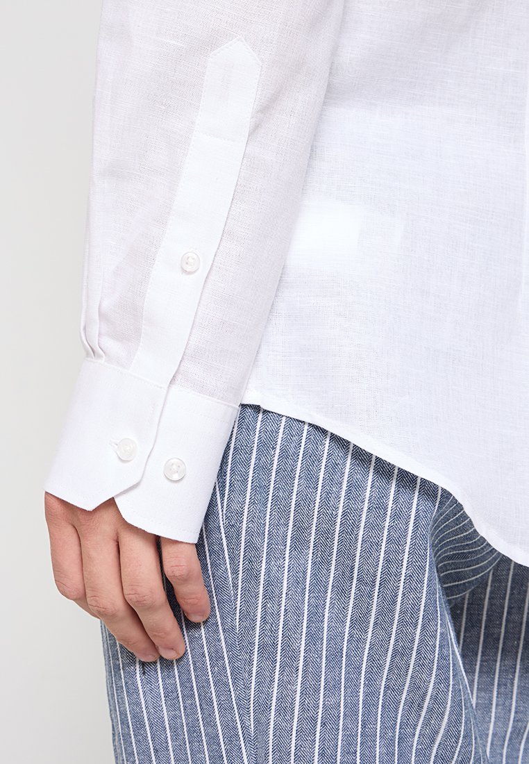Biała lniana mankietka koszuli z wygiętym wzorem i dwoma okrągłymi guzikami, w połączeniu z niebieskimi spodniami w paski w wzór jodełki.