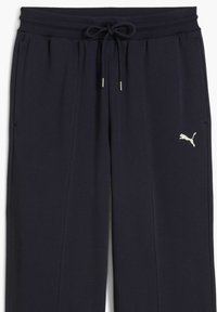 Mørkeblå sweatpants lavet af blødt materiale, med snøre i taljen, sidelommer og et lille sølvlogo på venstre ben.