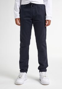 Marineblauwe, lichte rechte broek met een elastische tailleband en trekkoord, gecombineerd met witte sneakers. Soepele stofstructuur.