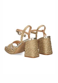 Sandalias con tiras y tacón de cuerda trenzada, con un acento metálico. El color es dorado claro con un acabado texturizado. Cierre de hebilla ajustable.